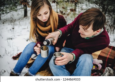 Portrait of happy young couple at the picnic on the Valentines Day in a snowy park. Man and girl pour into cups of mulled wine, hot tea, coffee with thermos. Christmas holiday, celebration. - Powered by Shutterstock