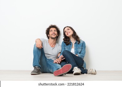 Portrait Of Happy Young Couple Sitting On Floor Looking Up Ready for your text or product