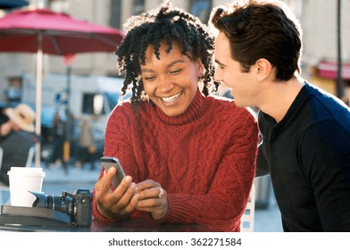 Portrait of happy young couple sitting ouside the cafeteria with smartphone. Close up of couple smiling and looking at mobile phone sitting on table in a coffee bar. Smiling couple having coffee. 
 - Powered by Shutterstock