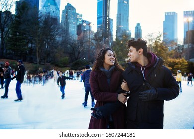 Portrait of a happy young couple smiling, holding hands and looking at each other while ice skating outside in Central Park, NYC - Powered by Shutterstock