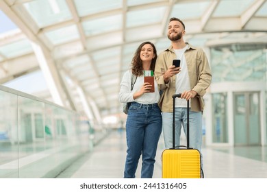 Portrait Of Happy Young Couple Standing At Airport Terminal With Luggage And Smartphone, Excited Millennial Man And Woman Air Travelling Together, Ready For Vacation Trip, Copy Space
