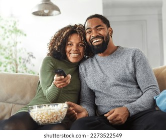 Portrait of a happy young couple watching tv together at home. Shot of a couple resting on the couch watching television - Powered by Shutterstock