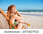 Portrait of happy young curvy woman with red hair and freckle in swimsuit relaxing on deck chair at beach while looking away. Carefree happy young woman sunbathing and relaxing at sea with copy space.