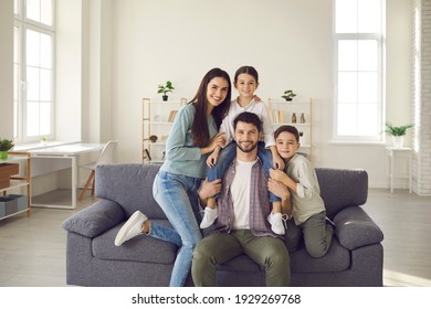 Portrait of happy young family with kids at home. Cheerful mother, father and little children smiling and looking at camera, sitting on sofa in the living-room of their new house or apartment