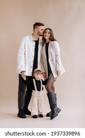 Portrait of a happy young family, with a little adorable daughter. Caring parents hold and gently hug their baby. Together they pose for a photo on beige background. Family concept - Shutterstock ID 1937339896