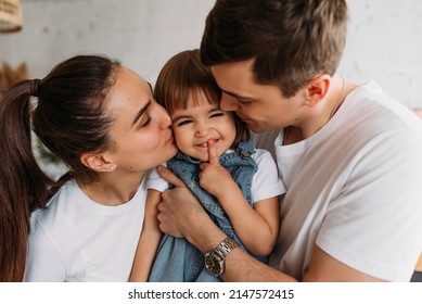 Portrait Of A Happy Young Family. Happy Family Mother, Father, Little Daughter. A Happy Young Family Spends Time Together In A Home Interior. Mom And Dad Kiss Their Baby. Happy Child With Parents