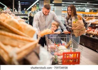 Portrait of happy young family  shopping for groceries in supermarket together with little boy, while choosing fresh bread loaf in bakery department - Powered by Shutterstock