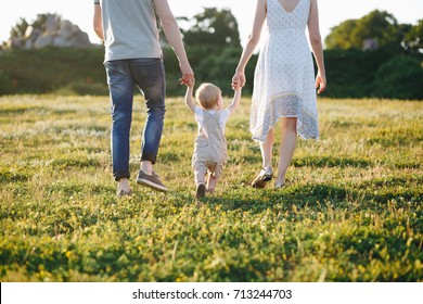 Portrait of a happy young family teaching baby to walk in the park