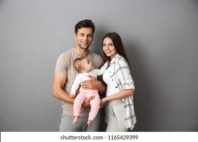 Portrait Of A Happy Young Family With Their Little Baby Girl Isolated Over Gray Background