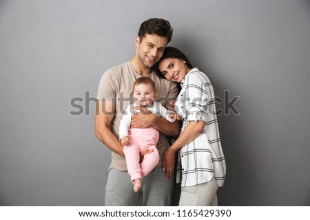 Portrait of a happy young family with their little baby girl isolated over gray background, hugging