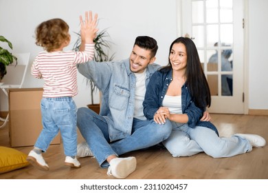 Portrait Of Happy Young Family With Toddler Child Celebrating Moving Day, Cheerful Parents Giving High Five To Their Cute Little Son While Sitting Together On Floor Among Cardboard Boxes - Shutterstock ID 2311020457