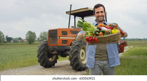 Portrait of a happy young farmer holding fresh vegetables in a basket. background of a tractor and nature Concept biological, bio products, bio ecology, grown by own hands, vegetarians, salads healthy