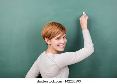 Portrait happy young female professor writing chalkboard while looking over shoulder