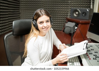 Portrait Of Happy Young Female Radio Presenter At Sound Studio With Sound Mixed Console And Microphone