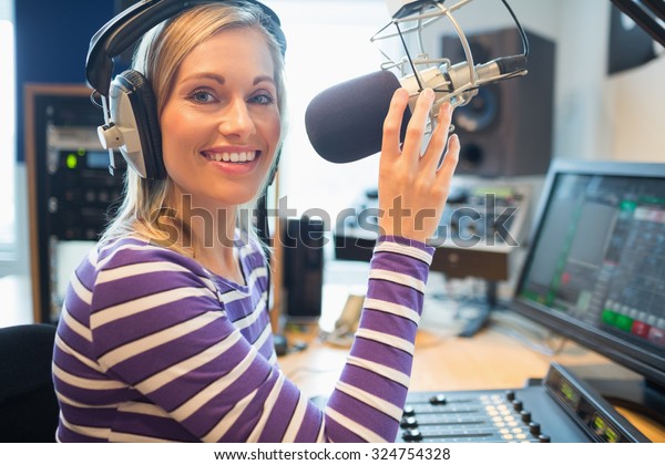 Portrait of happy young female radio host\
broadcasting in studio