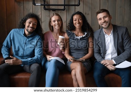Portrait of happy young four diverse multiracial people sitting in queue on sofa with papers and gadgets in hands, waiting for examination or job interview, hr management, corporate staffing concept.