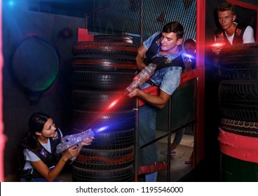 Portrait of happy young friends playing laser tag  game  with laser guns near tires in dark room 