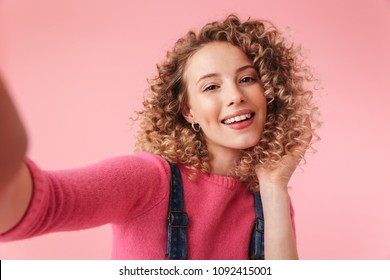 Portrait of happy young girl with curly hair taking a selfie isolated over pink background - Powered by Shutterstock