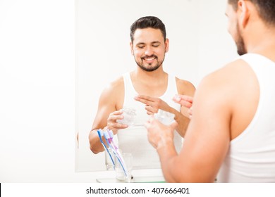 Portrait Of A Happy Young Hispanic Man Styling His Hair With Some Gel In Front Of A Mirror In The Bathroom