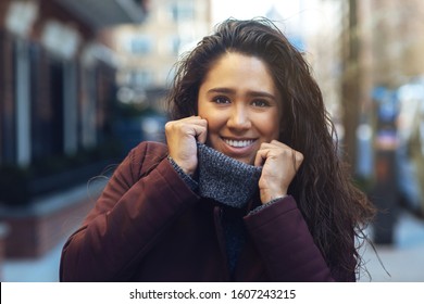 Portrait of a happy young hispanic woman smiling and holding  her sweater while walking outside on a sunny day