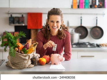 Portrait Of Happy Young Housewife Putting Money Into Piggy Bank After Shopping On Local Market