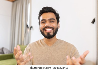 Portrait Of Happy Young Indian Guy Sitting At Desk And Gesturing. Smiling Ethnic Man Involved Virtual Meeting. Hispanic Male Student Taking A Part In Educational Conference