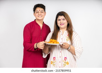 Portrait Of Happy Young Indian Mother And Son Wearing Traditional Outfit Holding Plate Full Of Laddu Or Laddoo Sweets Celebrating Diwali  Festival Together Isolated On White Background