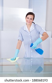 Portrait Of Happy Young Maid Cleaning Glass Table At Home