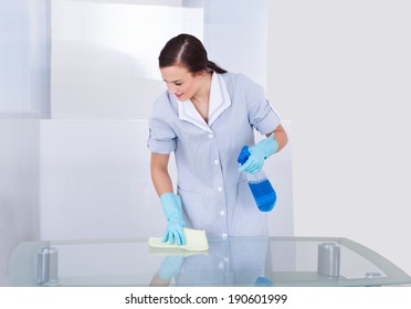 Portrait Of Happy Young Maid Cleaning Glass Table At Home