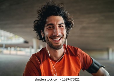 Portrait Of Happy Young Male Runner With Earphones In His Ears Looking At Camera Outdoor Smiling - Excited Fit Male