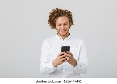 Portrait of a happy young man with curly hair isolated over white background, using mobile phone