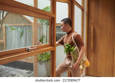 Portrait Of Happy Young Man Holding Mesh Bag Of Fresh Groceries When Leaving Shop