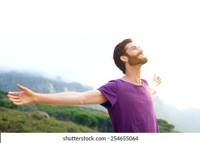 Portrait of a happy young man standing in nature with arms spread open