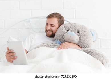 Portrait of a happy young man with a teddy bear while resting on a bed at home
