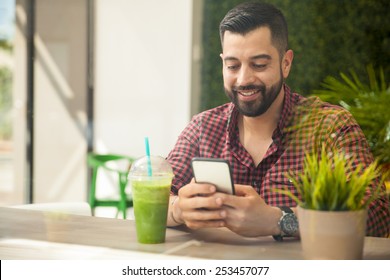 Portrait Of A Happy Young Man Using A Smartphone While Drinking A Healthy Smoothie