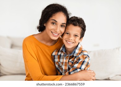 Portrait Of Happy Young Mom Embracing Her Kid Son Smiling To Camera At Home Interior. Boy Enjoying Mother's Hug Sitting On Couch Indoors. Family Bonding And Motherhood Concept - Powered by Shutterstock