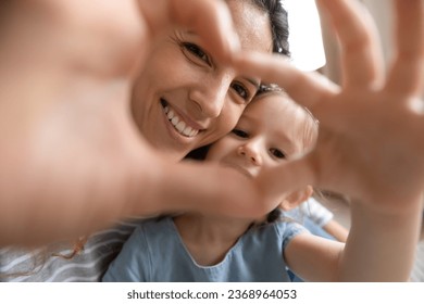 Portrait of happy young mother and small preschooler daughter look at camera posing making heart hand gesture, smiling millennial mom and little girl child show love and affection take selfie together