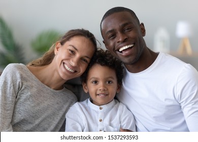 Portrait of happy young multinational family with preschooler biracial boy child posing at home, smiling international parents and mixed race ethnicity little son look at camera enjoy time together - Powered by Shutterstock