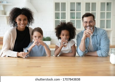 Portrait Of Happy Young Multiracial Family With Little Kids Drinking Pure Clean Mineral Water At Home, Smiling Multiethnic Parents With Small Daughters Children Recommend Healthy Lifestyle