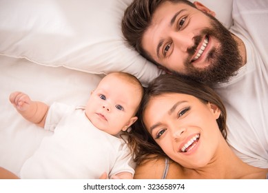 Portrait Of Happy Young Parents With Baby In The Bed At Home