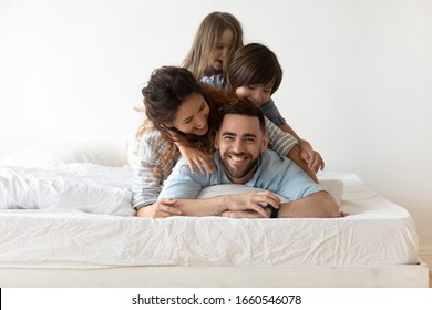 Portrait of happy young parents and small preschooler kids lying on white mattress in bedroom look at camera together, smiling family with little children relax on bed have fun, furniture concept - Powered by Shutterstock