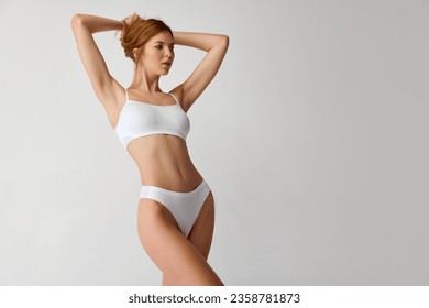 Portrait of happy young slim, fit beautiful lady wearing white underwear posing over grey color background. Concept of beauty, body and skin care, healthy eating, dieting, spa, anti-cellulite program