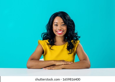 Portrait of a happy young smiling woman sitting behind desk  with arms crossed isolated on blue