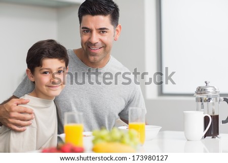 Portrait of happy young son with father having breakfast in the kitchen