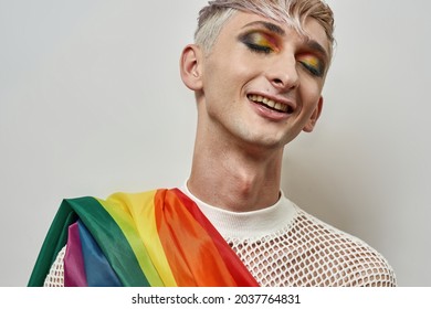 Portrait of happy young transgender with bright dark night party makeup on and colorful rainbow lgbtq flag posing with eyes closed isolated over white background. Beauty, lgbtqi, generation Z concept - Powered by Shutterstock