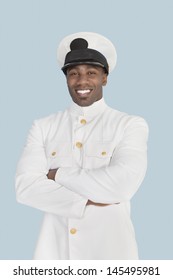 Portrait Of A Happy Young US Navy Officer Standing With Arms Crossed Over Light Blue Background