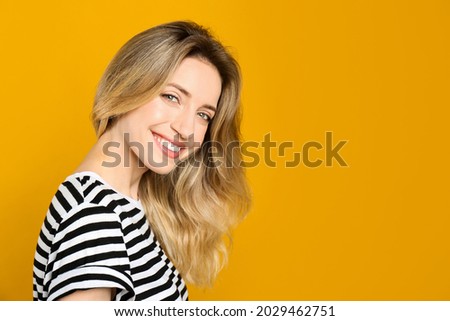 Portrait of happy young woman with beautiful blonde hair and charming smile on yellow background. Space for text