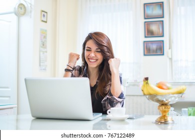 Portrait Of Happy Young Woman Celebrating Success With Arms Up In Front Of Laptop At Home.