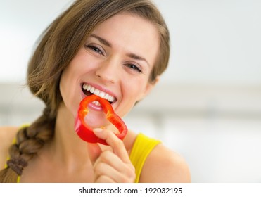 Portrait Of Happy Young Woman Eating Bell Pepper In Kitchen