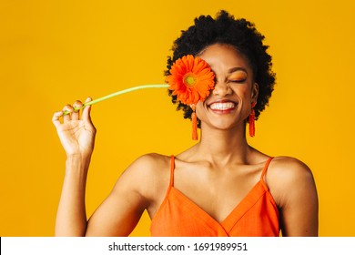 Portrait of a happy young woman holding orange Gerbera daisy covering her eye with eyes closed - Shutterstock ID 1691989951